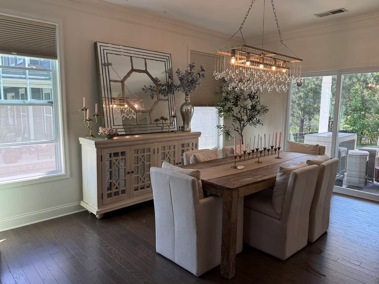 A dining room with a long wood table, white upholstered chairs and a crystal chandelier