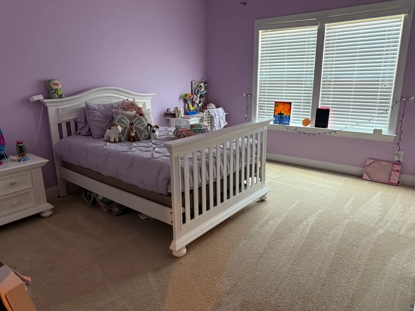 The same lilac bedroom after cleaning, with the bed made and the carpet freshly vacuumed