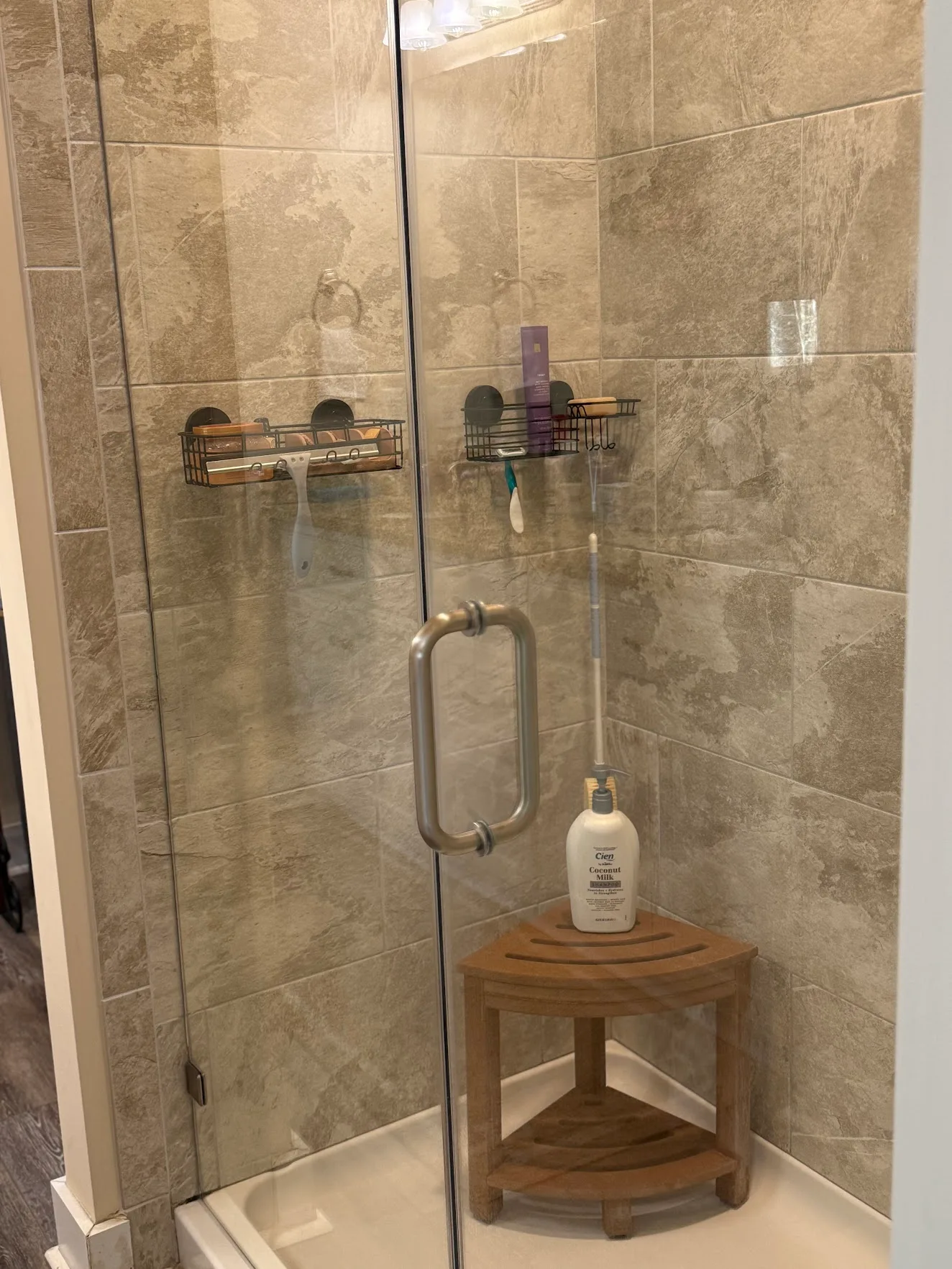 A clean walk-in shower with a glass door, stone-look tile and a wooden corner stool