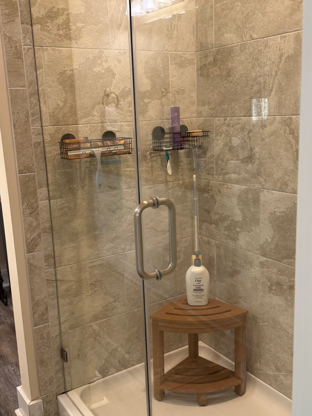 A clean walk-in shower with a glass door, stone-look tile and a wooden corner stool
